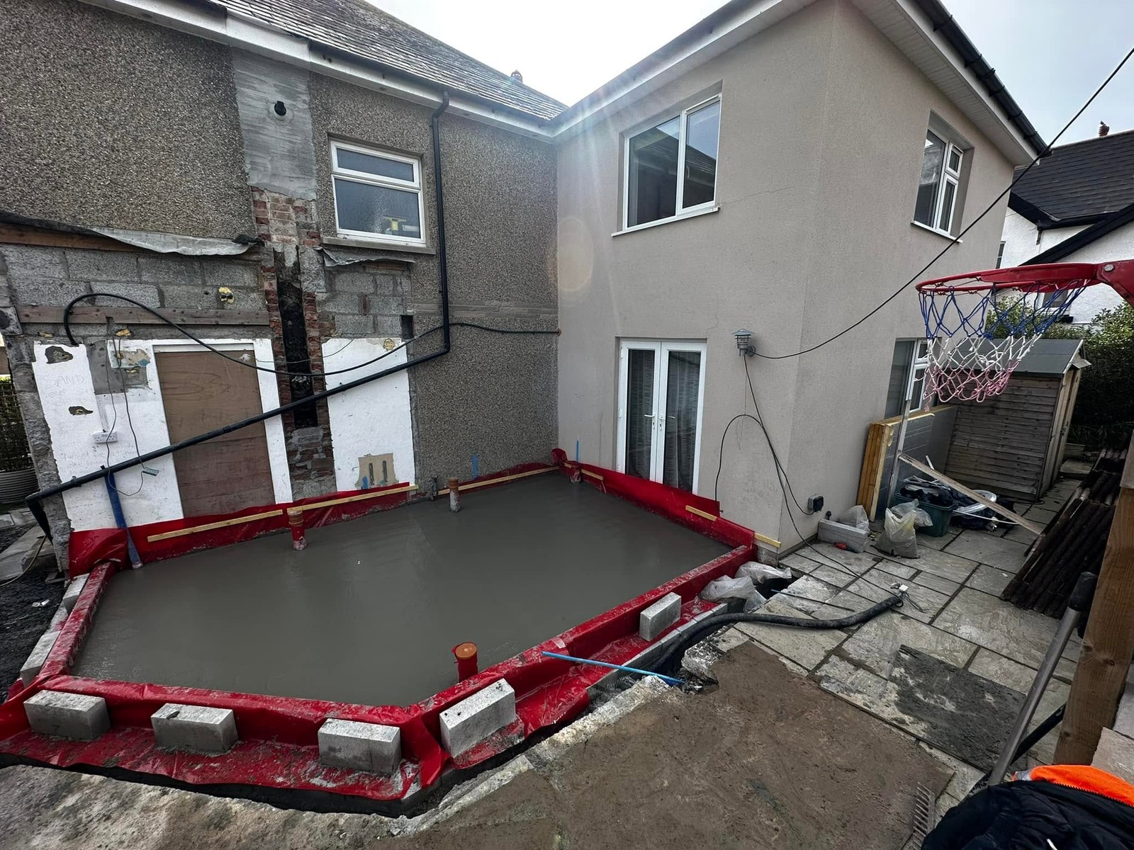 Fresh concrete base contained by red formwork beside a house