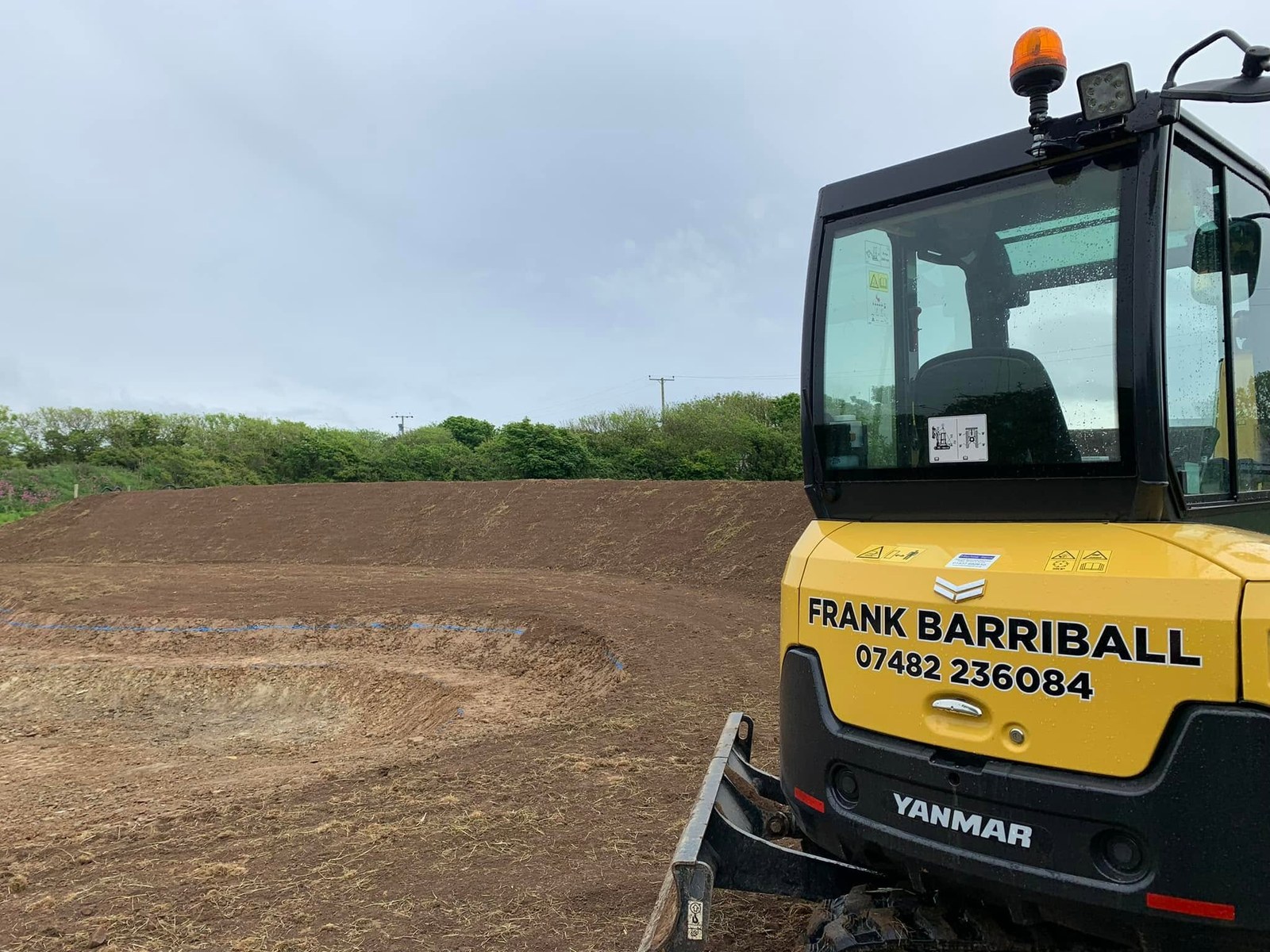 Frank Barriball branding on a yellow excavator beside prepared ground