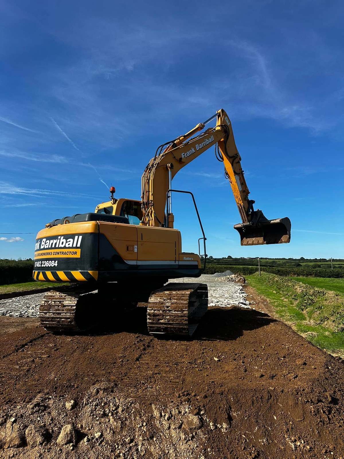Tracked excavator on a mound of earth under a blue sky